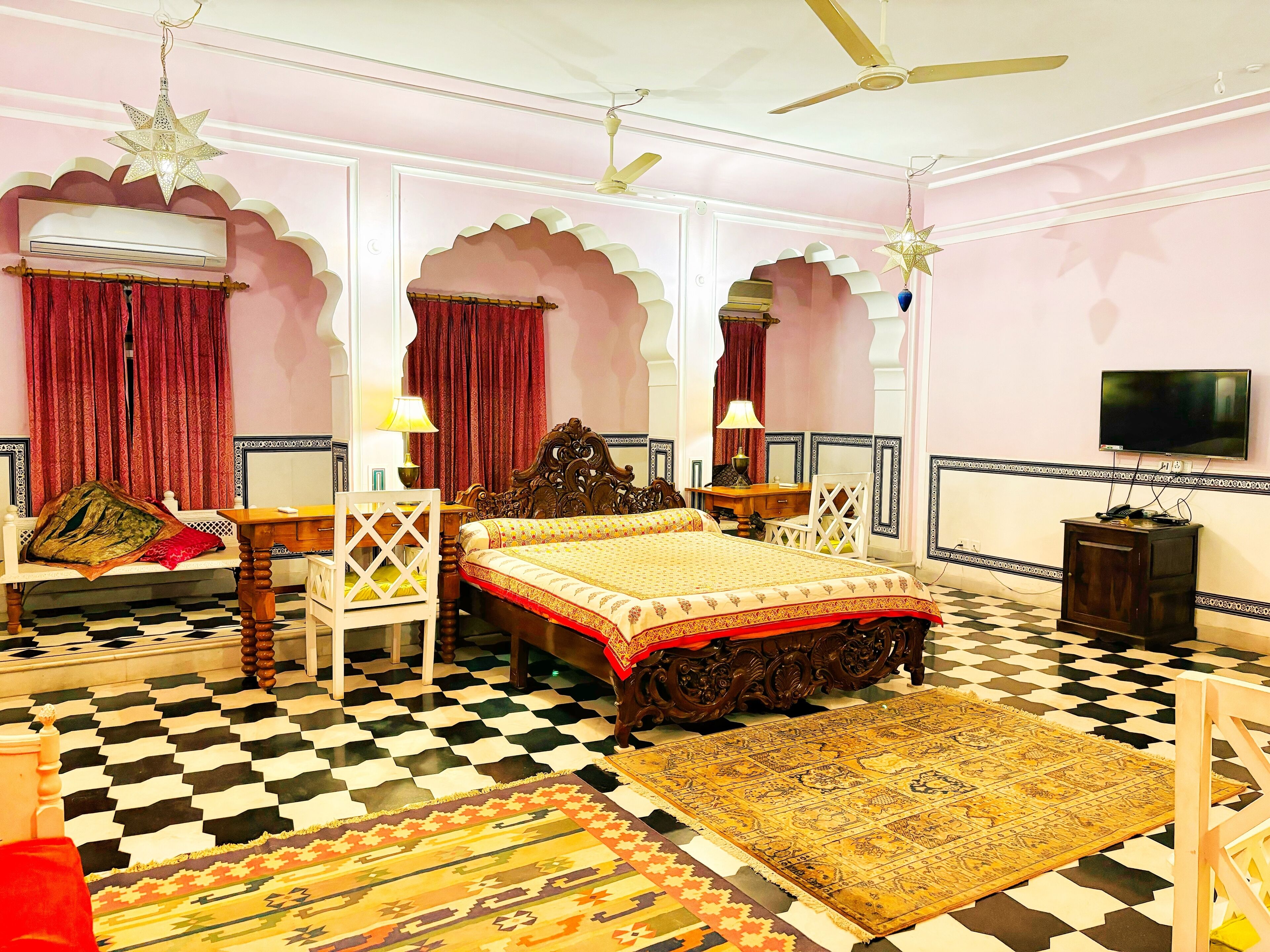 A traditional room with a bed, two chairs, a table, a television, and decorative elements like star-shaped lights and patterned rugs.