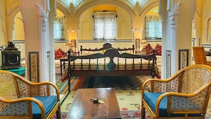 Una habitación tradicional con una cama de madera, dos sillas de mimbre, una mesita pequeña y decoración de pared ornamentada.