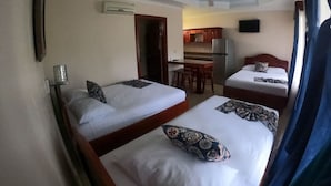 Ein Hotelzimmer mit zwei Betten, einer kleinen Küchenzeile, einem Deckenventilator und einer Klimaanlage.