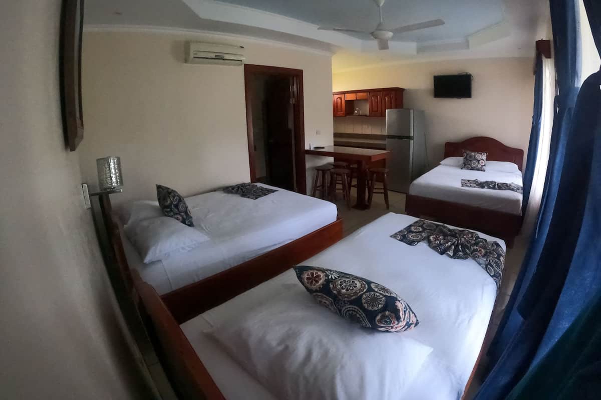 A hotel room with two beds, a small kitchenette, a ceiling fan, and an air conditioning unit.
