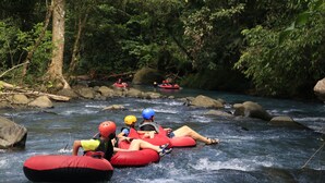Eine Gruppe von Menschen treibt mit Rafts auf einem Fluss, der von Felsen und Bäumen gesäumt ist.
