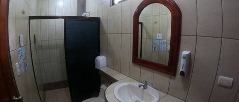 A bathroom with a toilet, sink, mirror, and a hand dryer.