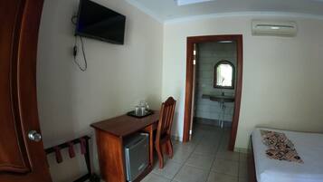 Habitació d'hotel amb un llit, una taula de treball amb un ordinador, un televisor penjat a la paret i un bany visible a través d'una porta oberta.