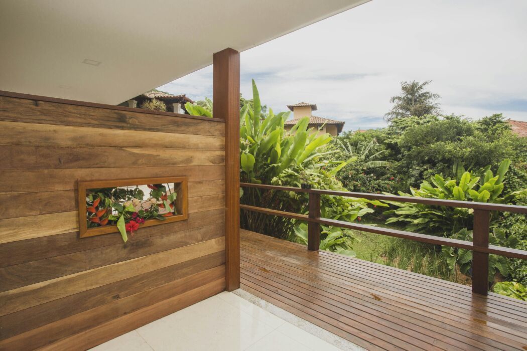A wooden deck with a railing, a framed picture of flowers, and lush greenery in the background.