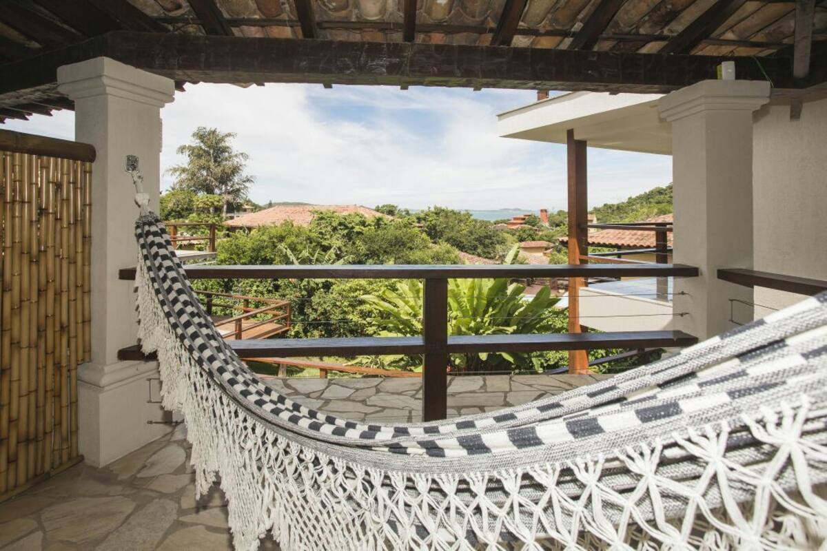 A hammock on a balcony with a view of greenery and buildings.