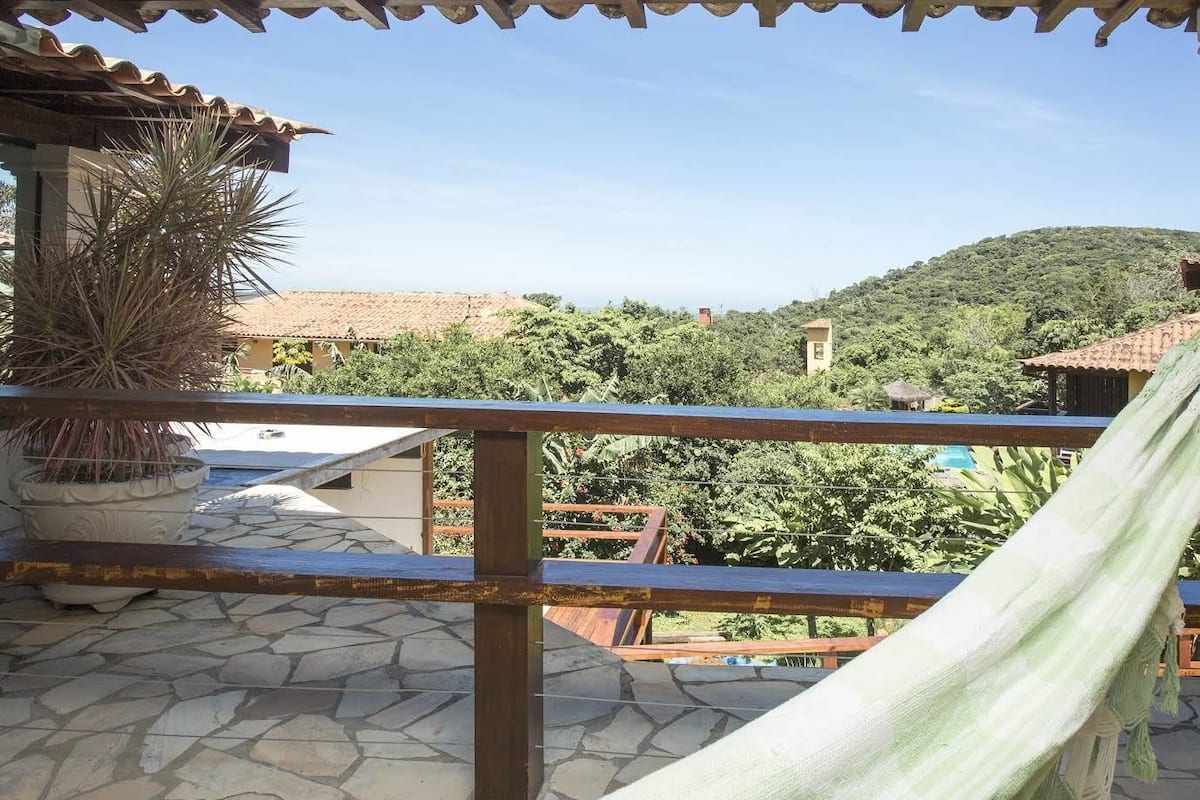 A balcony with a hammock, a potted plant, and a view of a hillside with buildings.