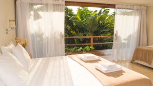 Ein Hotelzimmer mit einem großen Bett, einem Balkon mit Blick auf Grünflächen und einem Fenster mit transparenten Vorhängen.