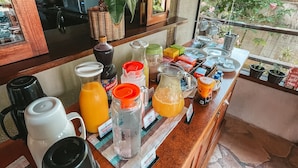 Ein Frühstücksbuffet mit verschiedenen Getränken und Speisen, einer Kaffeemaschine und Blick ins Freie durch ein Fenster.