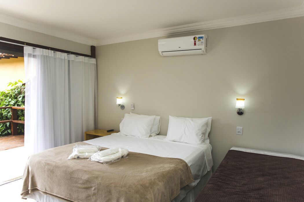 Une chambre d’hôtel avec un lit, deux lampes de chevet, un appareil de climatisation et une vue sur l’extérieur.