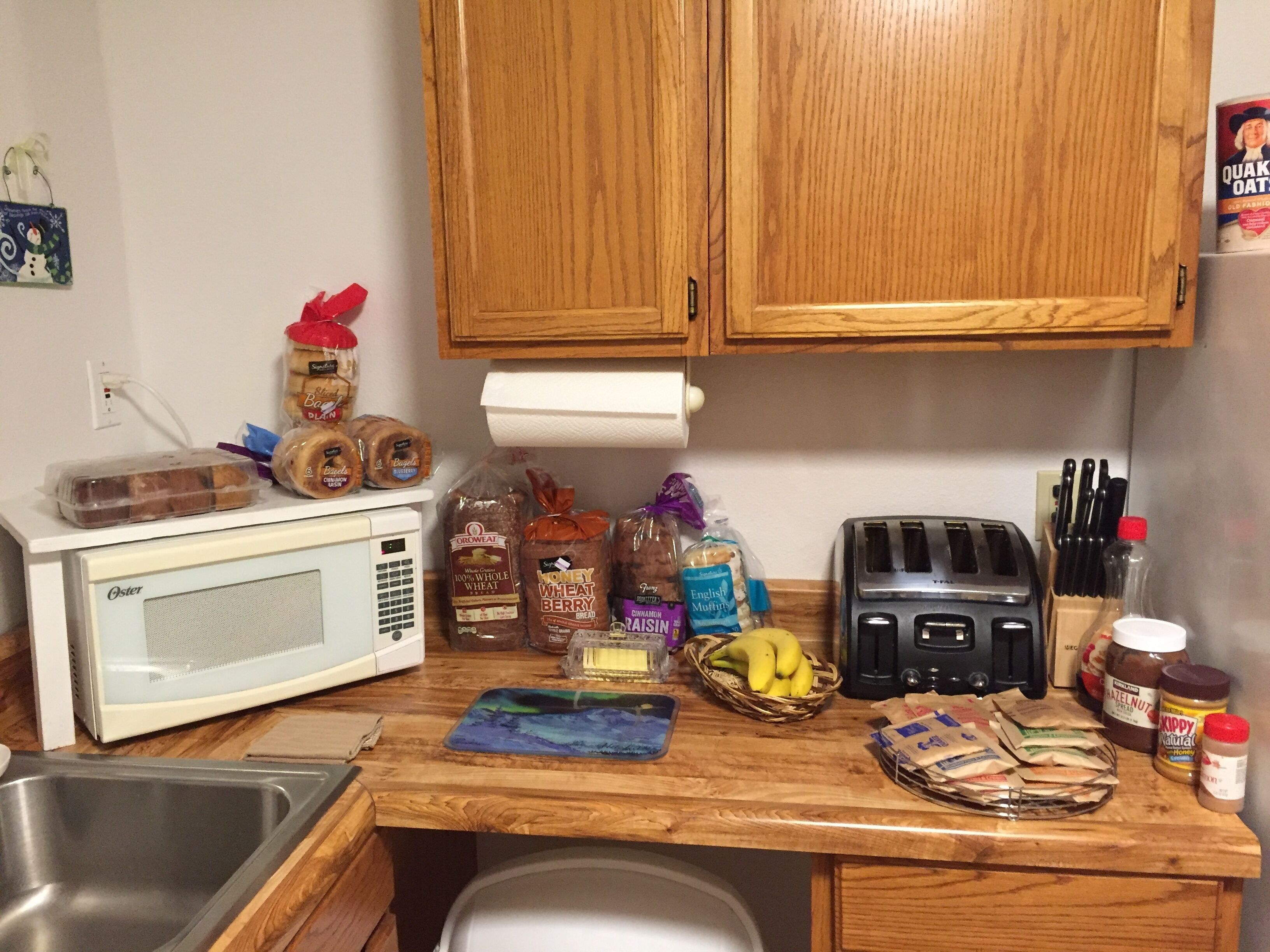 A kitchen with wooden cabinets, a microwave, toaster, and various food items on the counter.