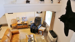 Un salon comprenant un canapé en cuir, une table basse avec des magazines, un fauteuil en cuir noir, une petite table avec une lampe et une tête d’animal empaillée accrochée au mur.