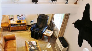 Un salon comprenant un canapé en cuir, un fauteuil massant, une table basse avec des magazines, une bibliothèque, un bureau avec un ordinateur et une tête d’animal montée au mur.