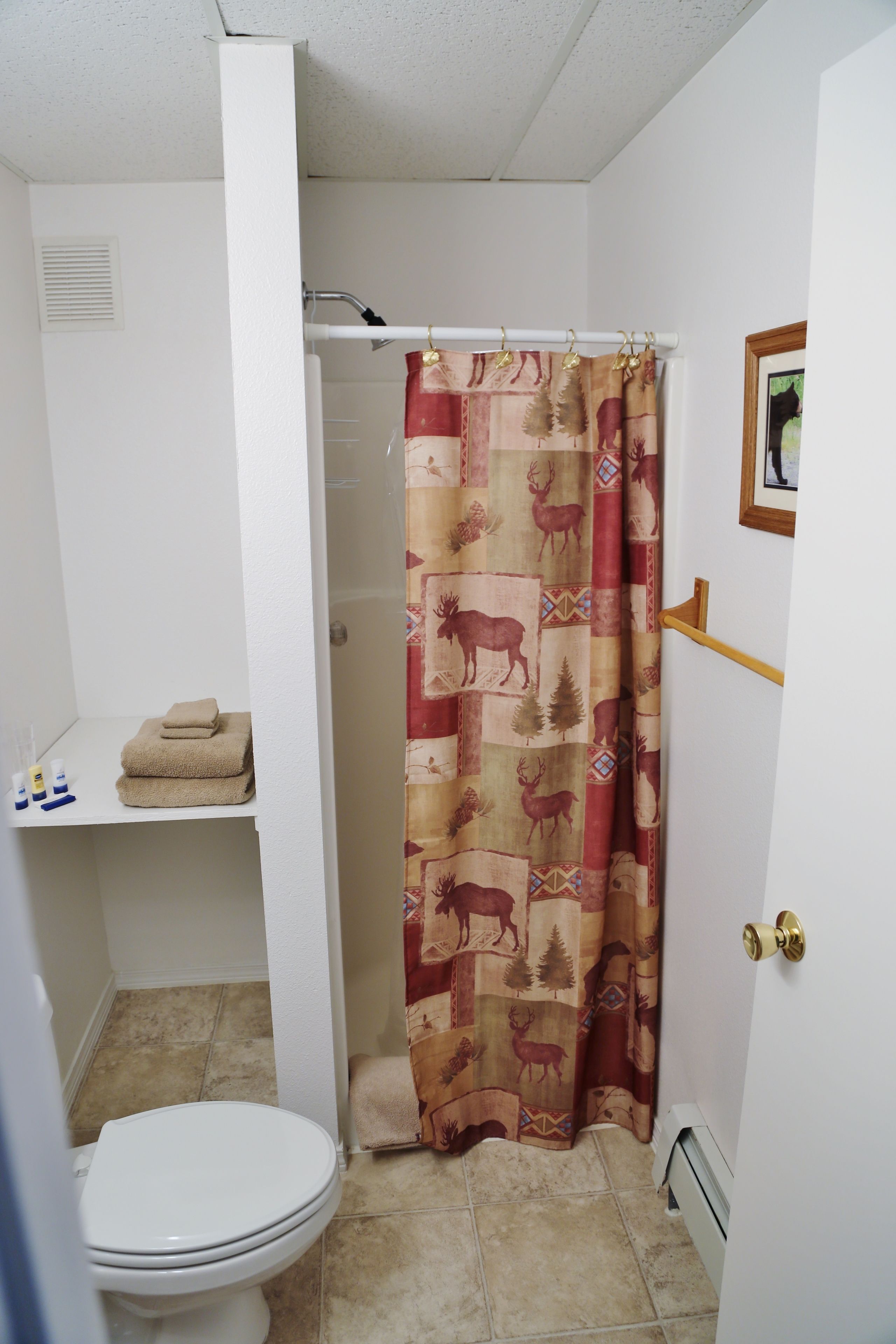 A bathroom with a toilet, a shower curtain with a deer pattern, and a towel rack with folded towels.