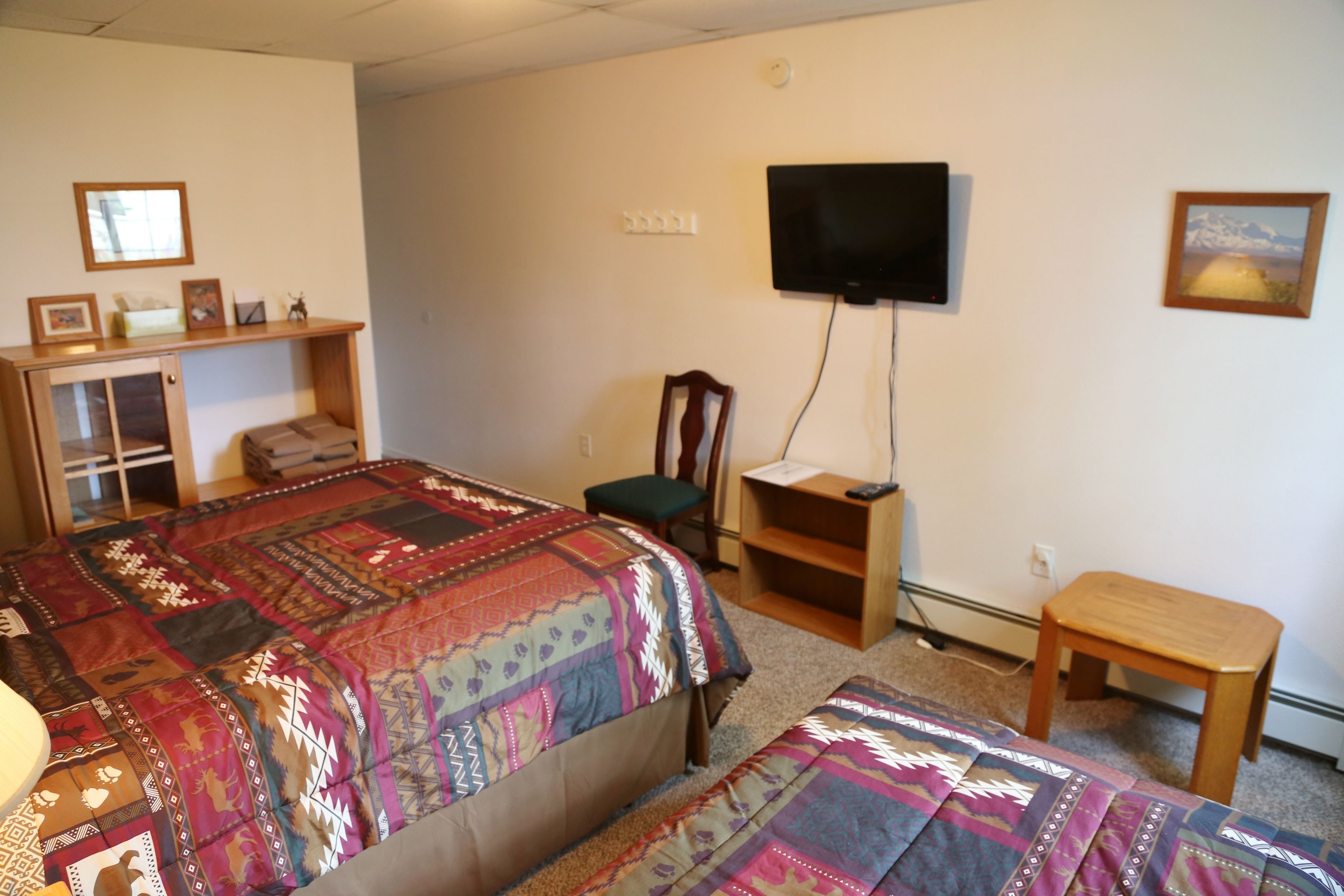 Ein Schlafzimmer mit einem großen Bett, einem Schreibtisch, einem Sessel, einem an der Wand montierten Fernseher und einem kleinen Tisch.