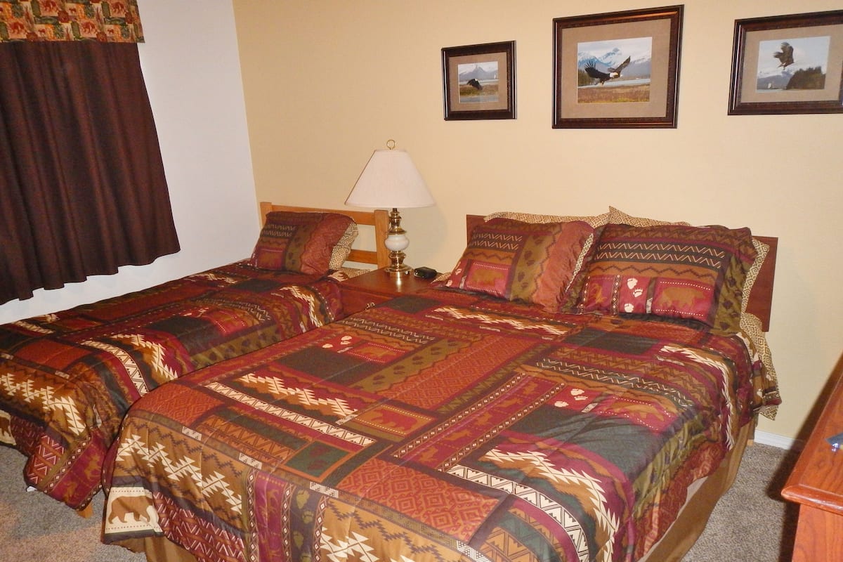 Una cama doble con una colcha estampada, una mesita de noche con una lámpara y tres cuadros enmarcados en la pared.