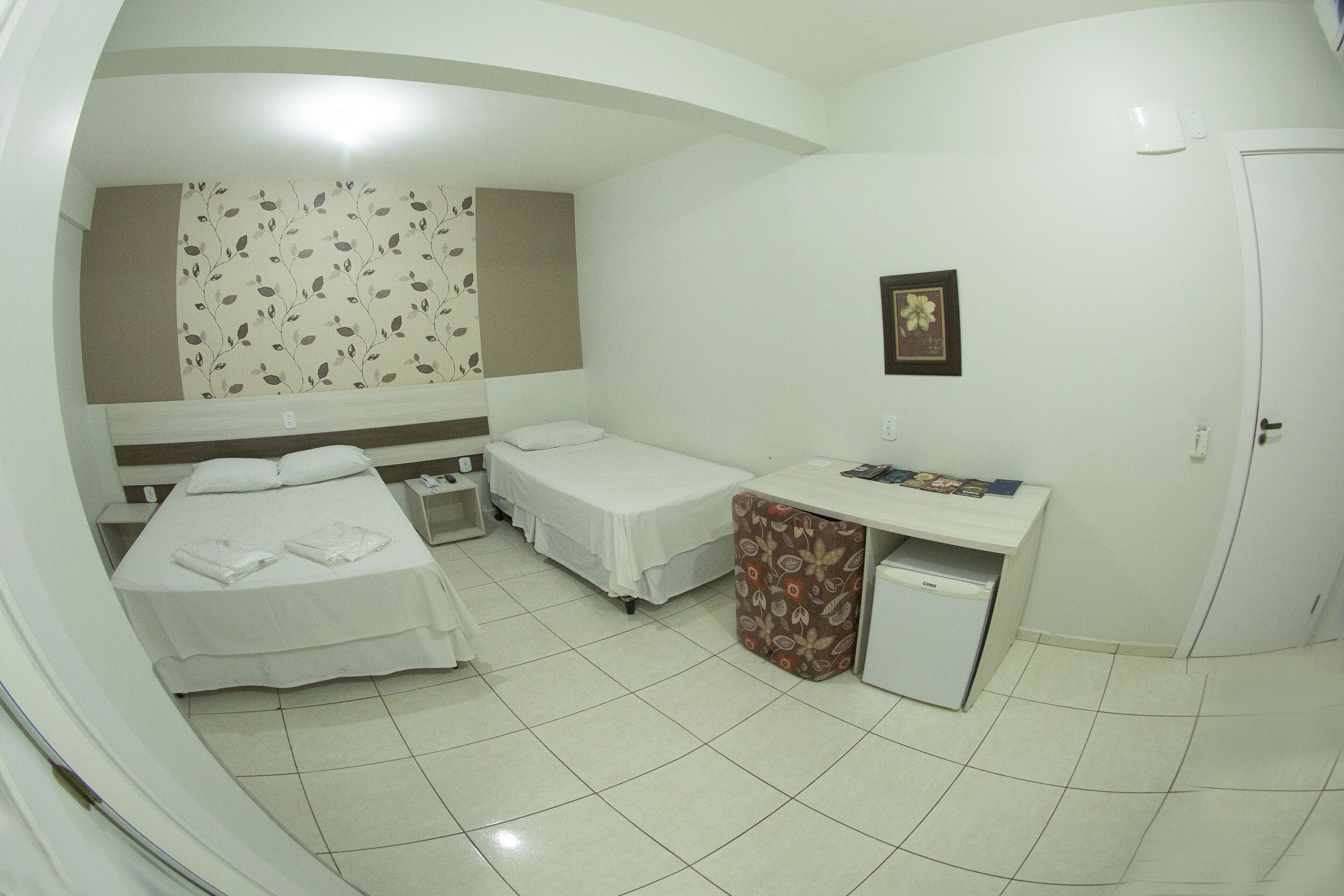 A hotel room with two beds, a desk, a small refrigerator, and a wall-mounted picture.