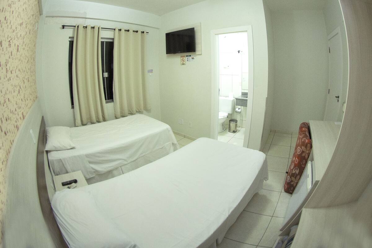 Une chambre d’hôtel avec deux lits simples, un téléviseur fixé au mur et une salle de bain visible à travers une porte ouverte.