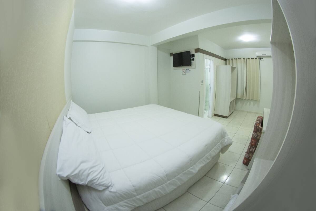 Une chambre d’hôtel avec un lit, un téléviseur fixé au mur et une salle de bain visible à travers une arche.