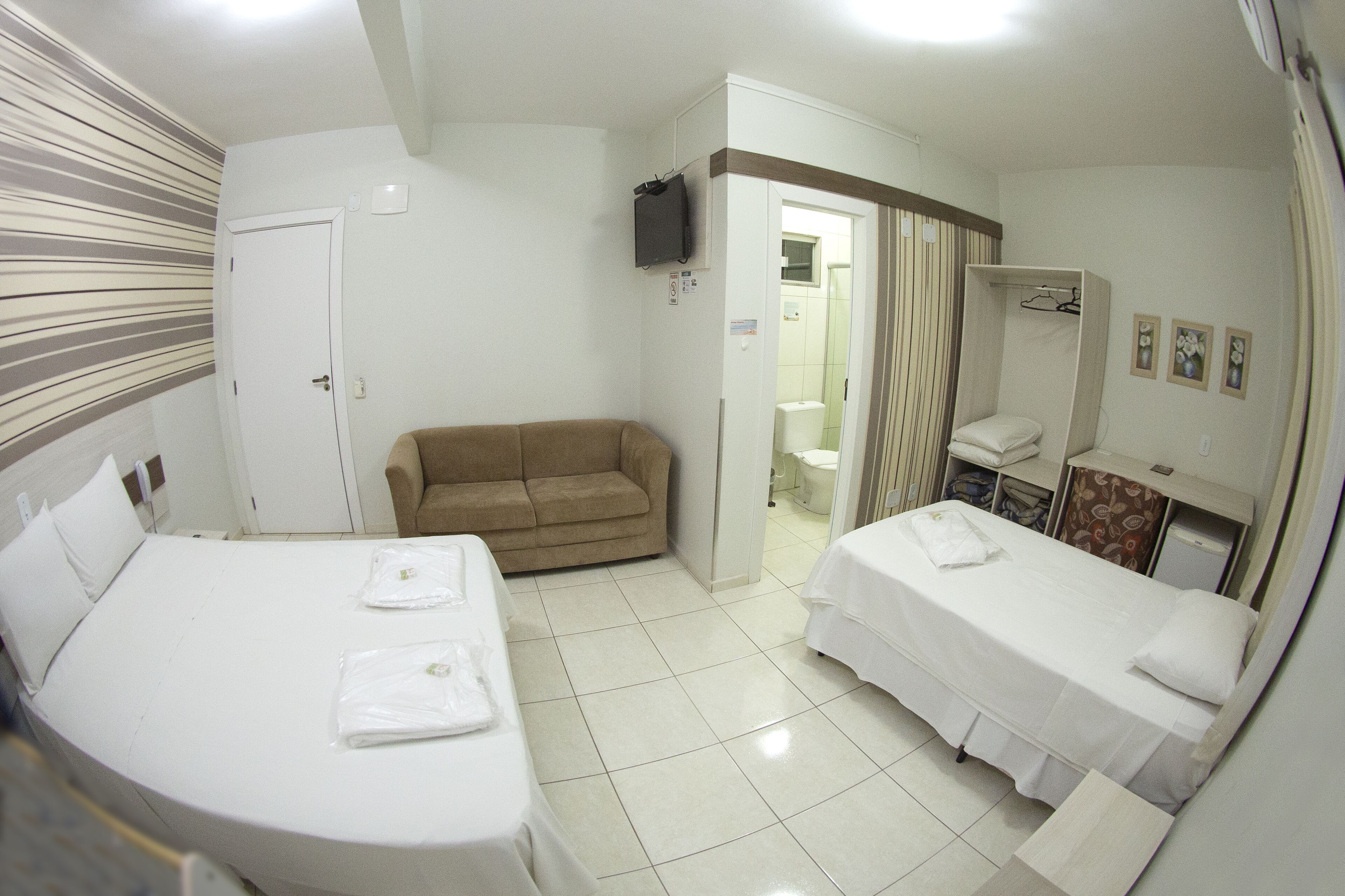 Une chambre d’hôtel avec deux lits, un canapé, une télévision, une salle de bain et un espace douche.