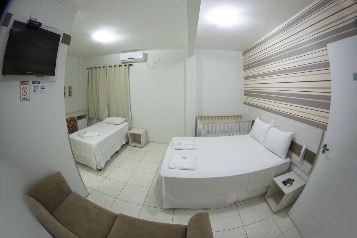 Une chambre d’hôtel avec un grand lit, un plus petit lit, un canapé, une télévision et un radiateur.