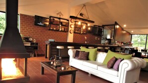 A cozy living room with a fireplace, a white sofa with cushions, a coffee table, and a brick wall. - Hotel Bambu Inn (Salento)