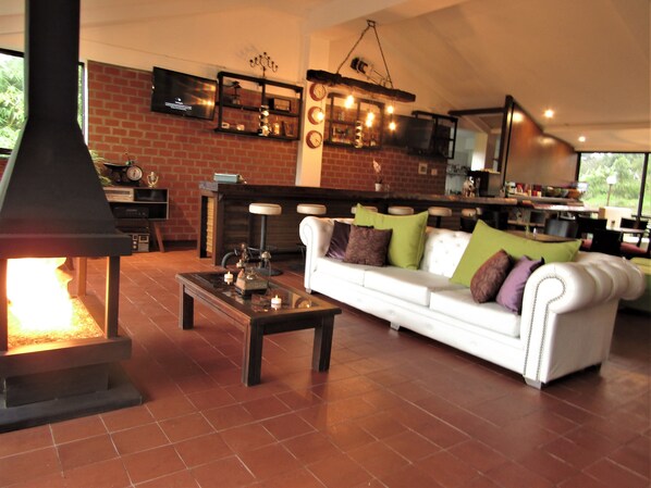 A cozy living room with a fireplace, a white sofa with cushions, a coffee table, and a brick wall.