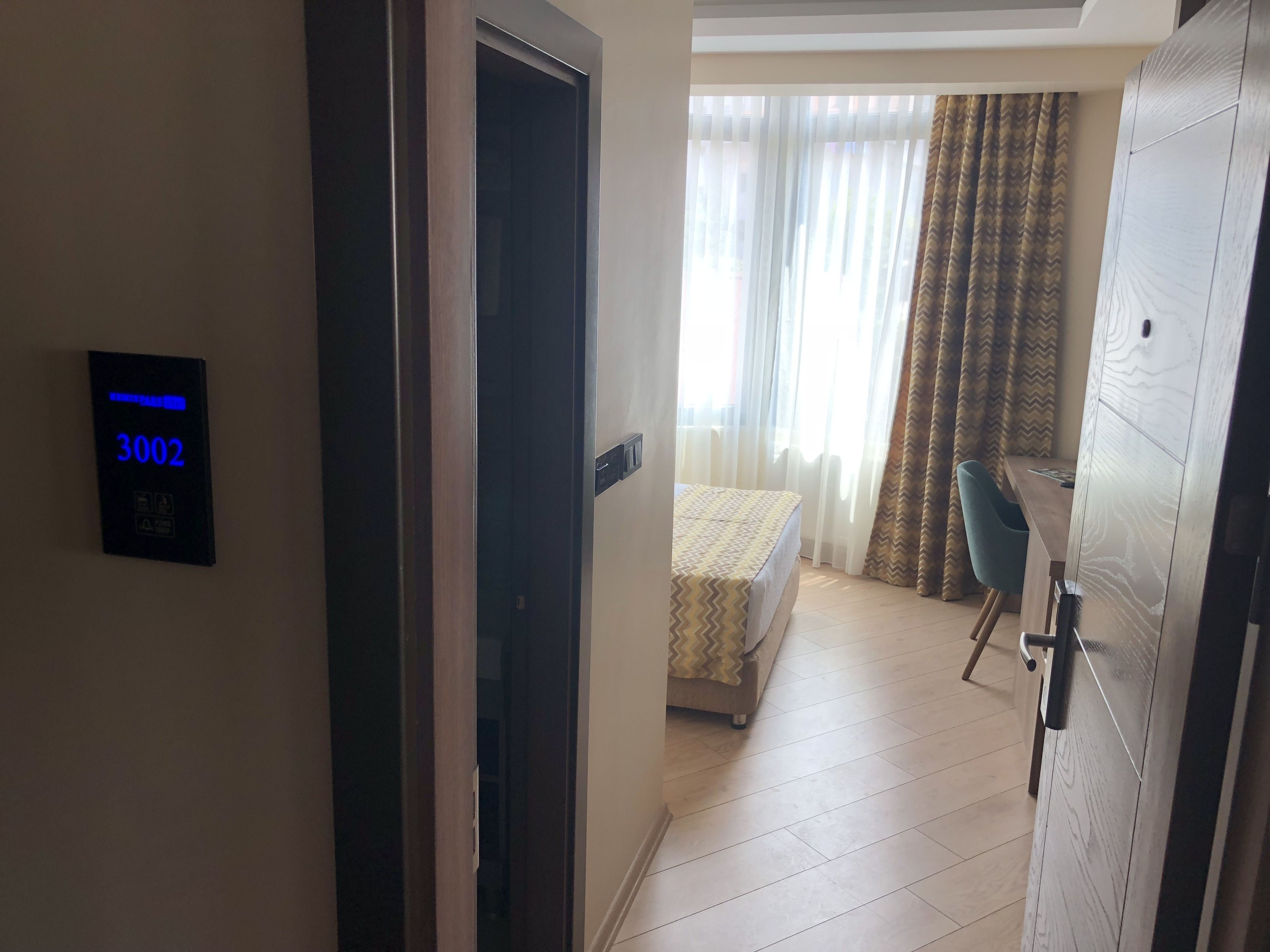 Une chambre d’hôtel avec un lit, un bureau et une vue sur l’extérieur à travers des rideaux transparents.