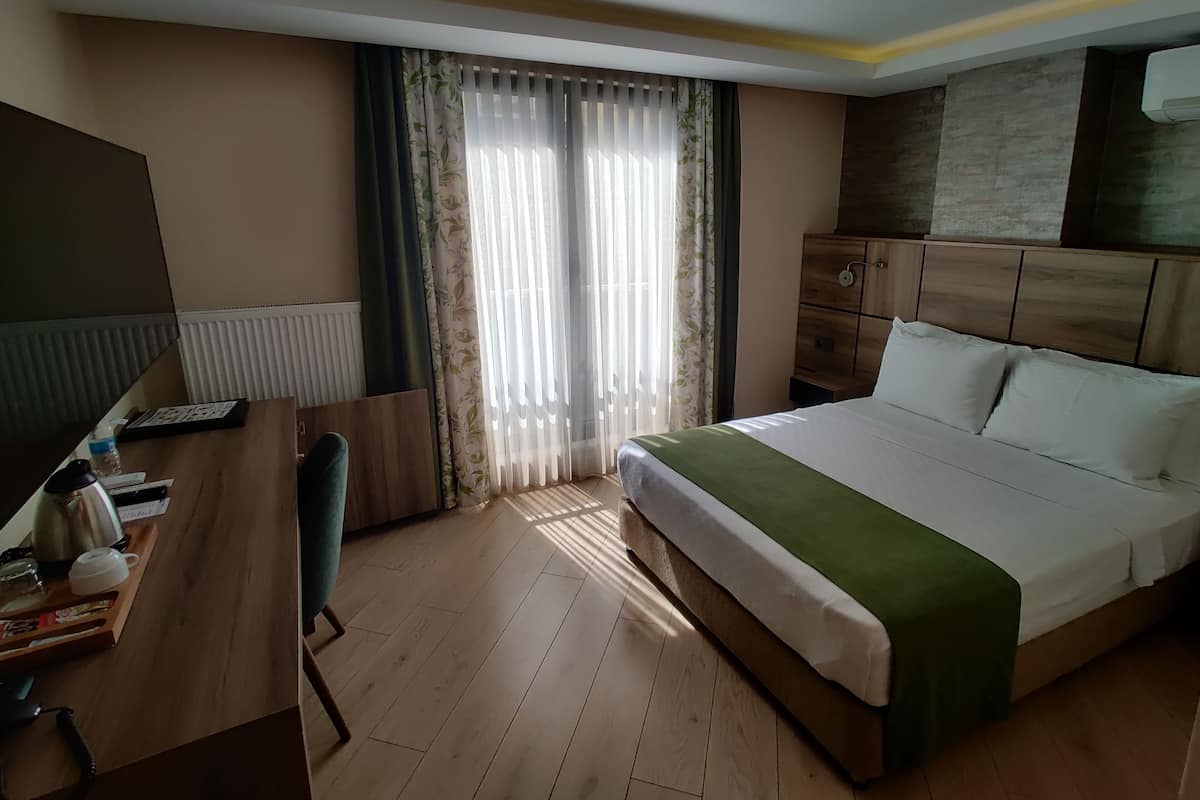Una habitación de hotel con un escritorio de madera, una cama con un edredón verde, un armario y un radiador.