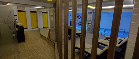 Un vestíbulo de hotel con un mostrador de recepción de madera, una zona de recepción y una piscina visible a través de un panel de vidrio.