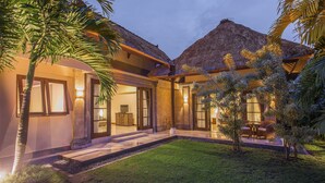 Una casa moderna con techo de paja, una entrada bien iluminada y un pequeño jardín con asientos.