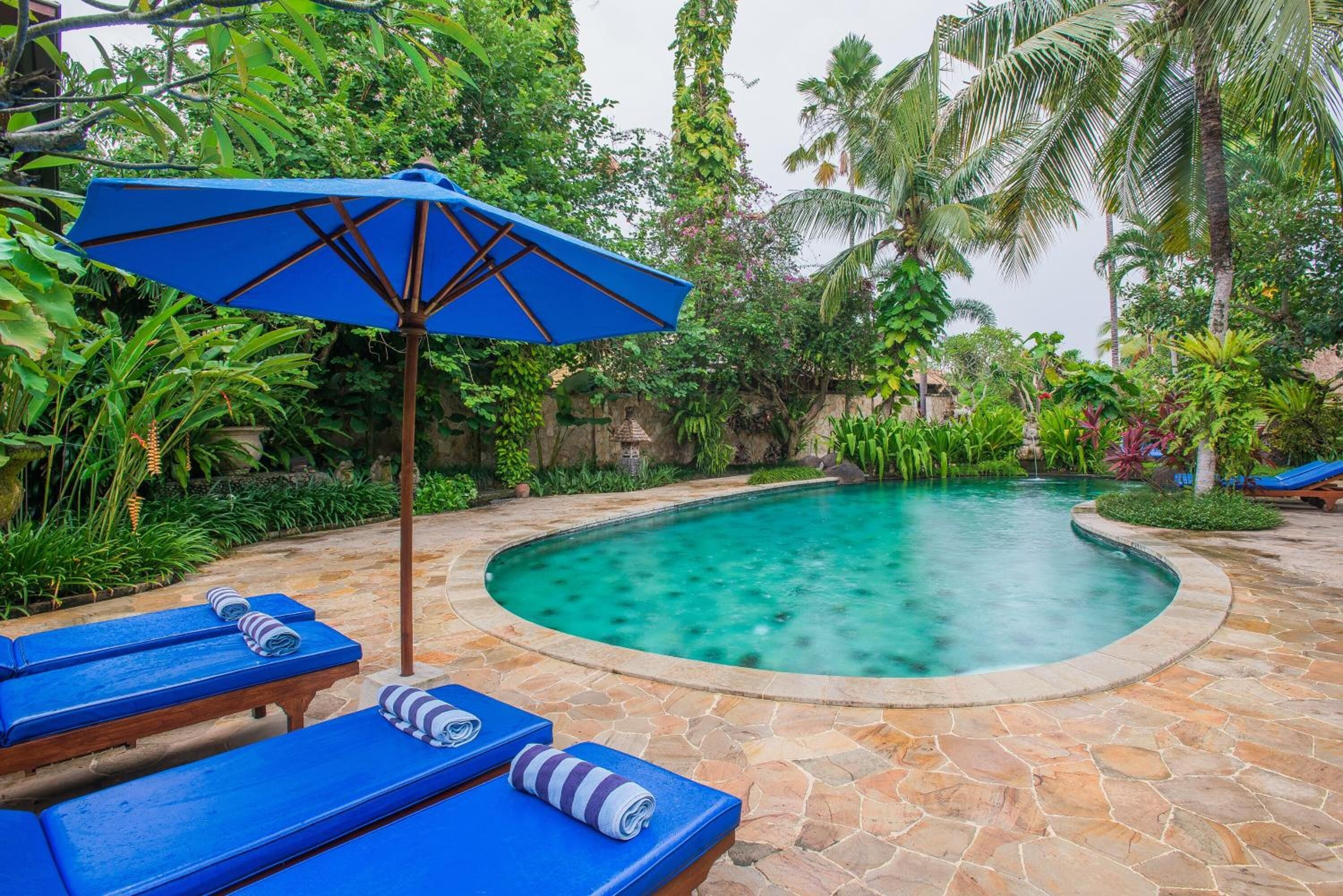 A swimming pool with blue lounge chairs and an umbrella.