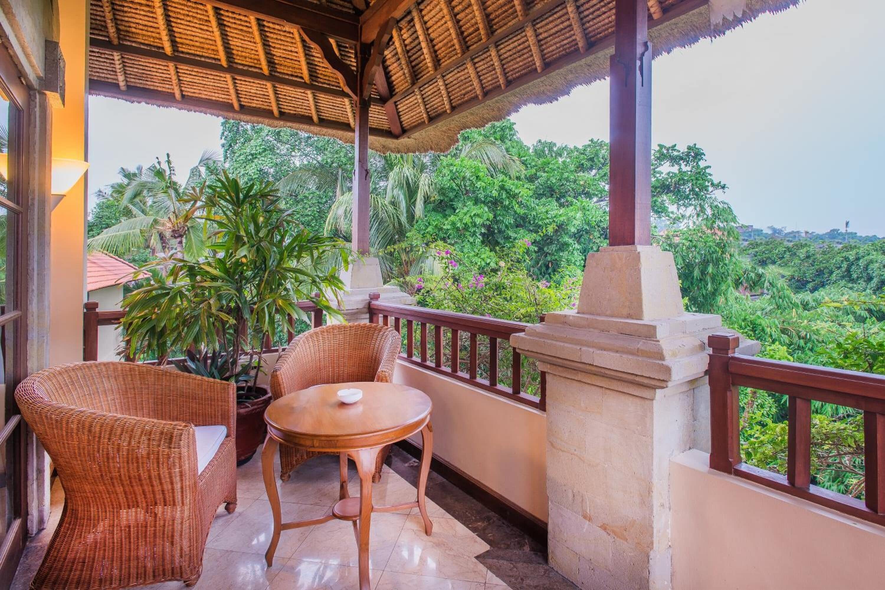 A balcony with wicker furniture, a potted plant, and a view of lush greenery.