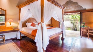 Una cama con dosel de cuatro postes, con cortinas blancas, un cabecero de madera y una mesita de noche de madera con una lámpara.