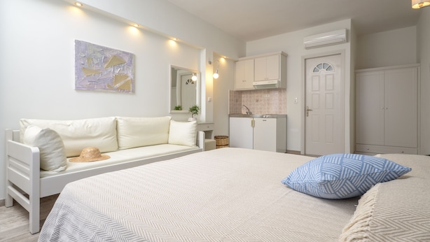 A bedroom with a bed, a sofa, a kitchenette, and a bathroom. - Blue Sky Summer (Naxos)