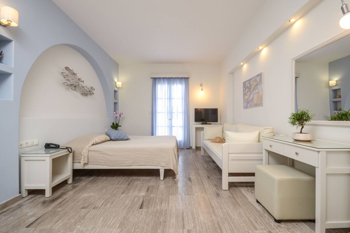 A modern bedroom with a bed, bedside table, TV, and a desk with a chair.