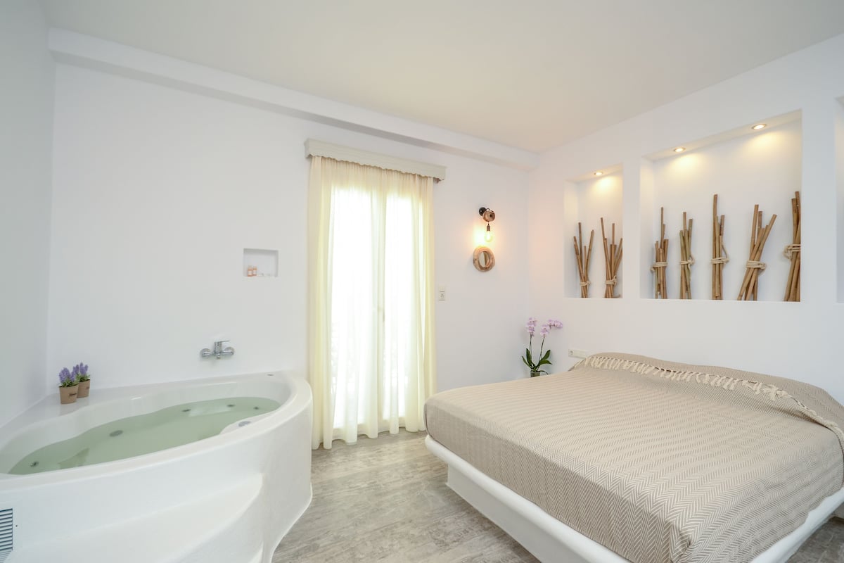 A modern bedroom with a large bed, a bathtub, and a wall-mounted light fixture.