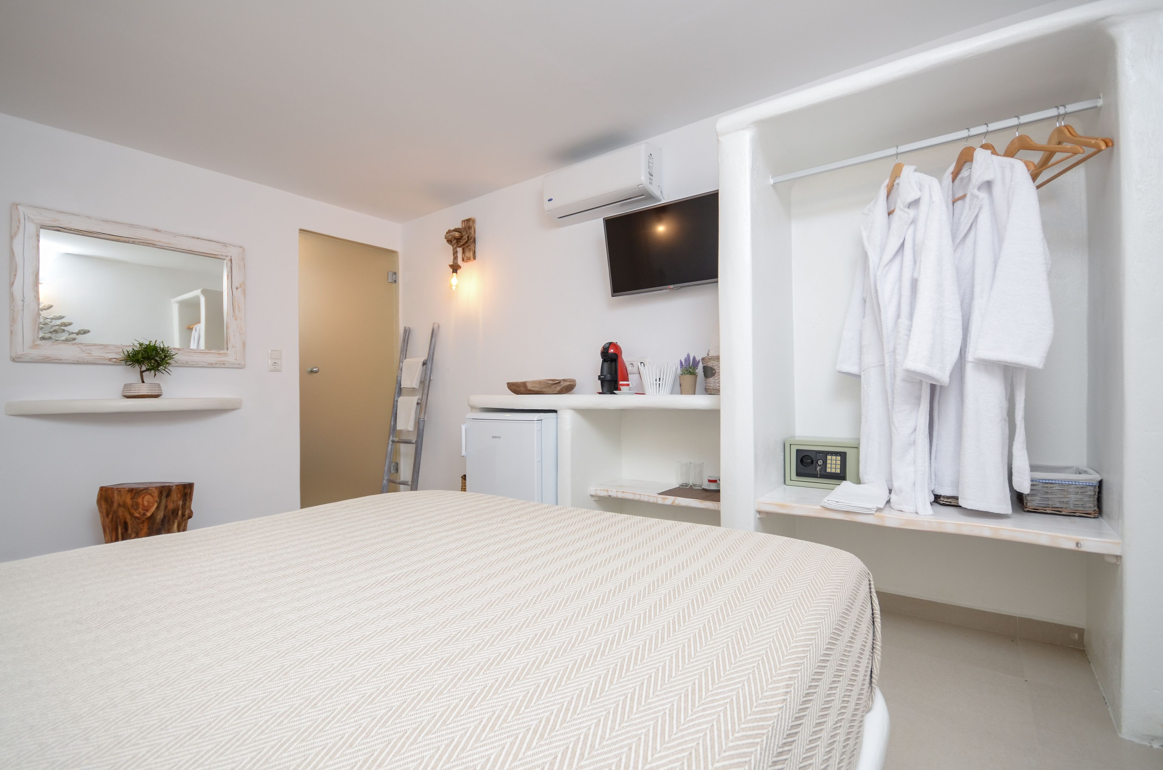 Une chambre moderne avec un grand lit, une armoire avec penderie, un petit coin cuisine, une télévision et un miroir.