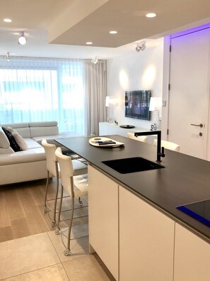 Una cucina moderna con isola centrale, TV integrata e zona pranzo con divano e sedie.
