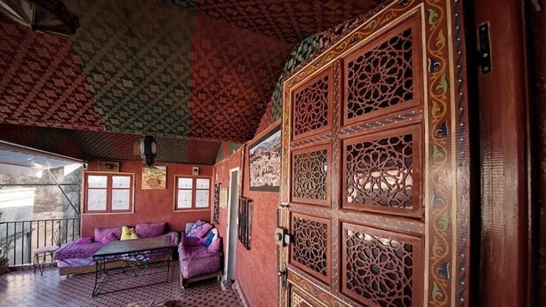 A room with a patterned ceiling, a large ornate wooden door, and a sofa with cushions. - Dar  El Amane Abqari (Fes)