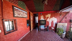 A room with a patterned floor, a television, a framed picture on the wall, and a mural of a camel. - Dar  El Amane Abqari (Fes)