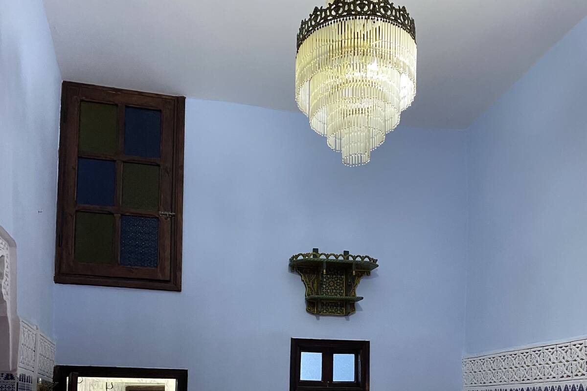 A bedroom with a bed, a nightstand, a mirror, a chandelier, and a window.