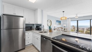 A modern kitchen with stainless steel appliances, a dishwasher, and a large island with a stovetop. - Coastal Escape Oceanfront Corner Unit with Heated Pool and Resort Amenities (Cocoa Beach)