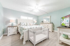 Une chambre à coucher comprenant un lit, un berceau, une commode, un miroir et un téléviseur.
