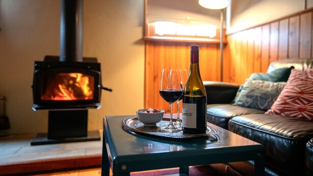 A cozy living room with a fireplace, a sofa, a table with a bottle of wine and glasses, and a television.
