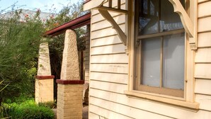 A wooden house with a red awning, a window with a wooden frame, and a garden with green plants and purple flowers.