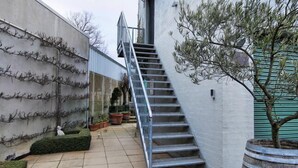 A staircase leading up to a building with a metal railing, surrounded by potted plants and a tree. - Bella Loft:  A studio apartment in the heart of Woodend. (Woodend)