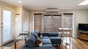 A modern living room with a sectional sofa, a dining table, and a TV. - Bella Loft:  A studio apartment in the heart of Woodend. (Woodend)