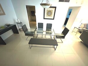 Un espace repas moderne avec une table à plateau en verre et des chaises noires, un banc et un luminaire suspendu.