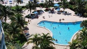 Un espace piscine aménagé dans un complexe hôtelier, comprenant une grande piscine, des chaises longues et des palmiers.