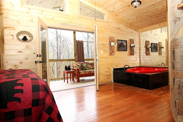 L’intérieur d’un chalet en bois comprend un lit, un canapé, une baignoire rouge et un balcon avec vue sur les arbres.
